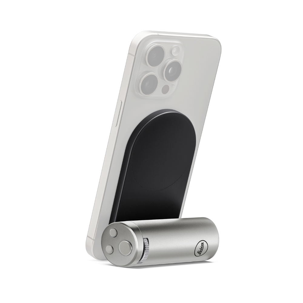 A silver cylindrical magnetic phone accessory with a visible MagSafe ring, shown attached to the back of a white smartphone on a clean white background.